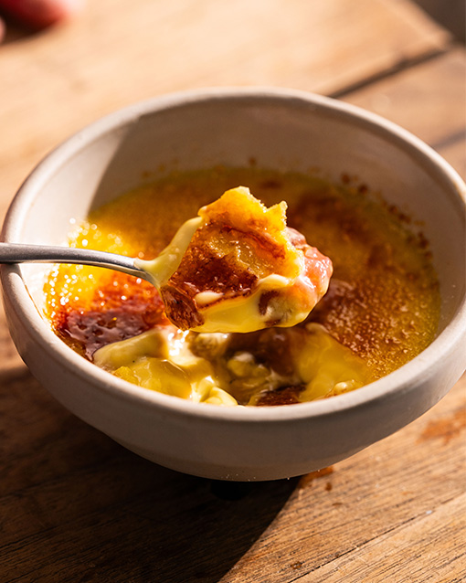 Rhubarb Creme Brûlée in a bowl, with a portion of it scooped out with a spoon.